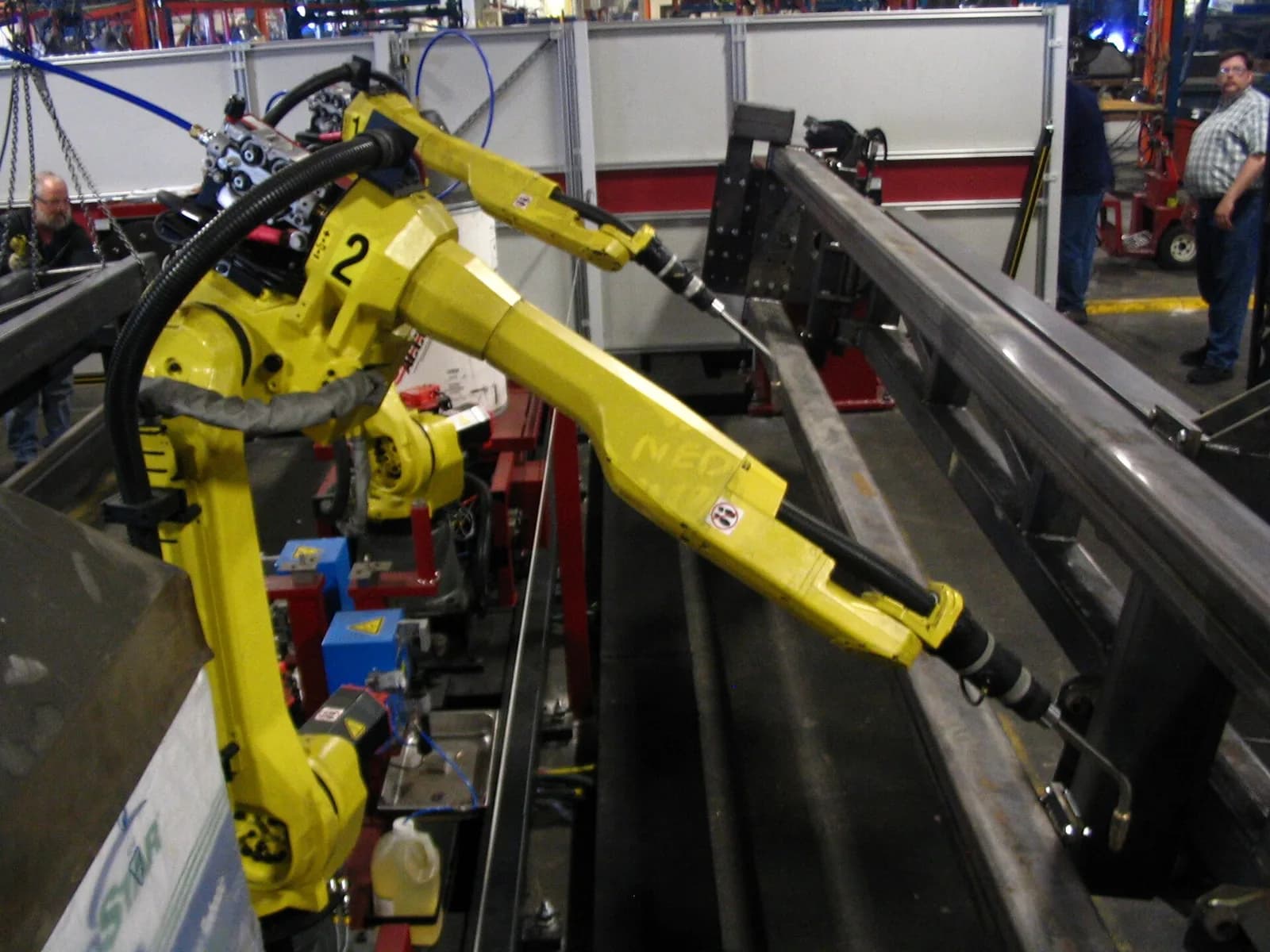 Шестиосевые роботы FANUC жёлтого цвета держат сварочные горелки над заготовкой в приспособлении