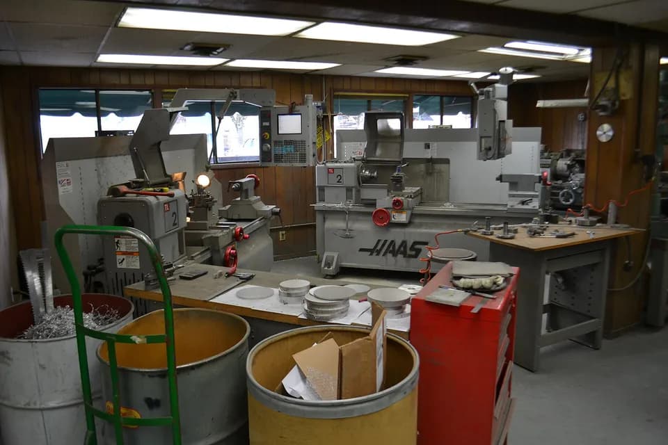 Два токарных станка Haas в мастерской, на переднем плане столы с алюминиевыми дисками-заготовками, бочки со стружкой и красная инструментальная тележка