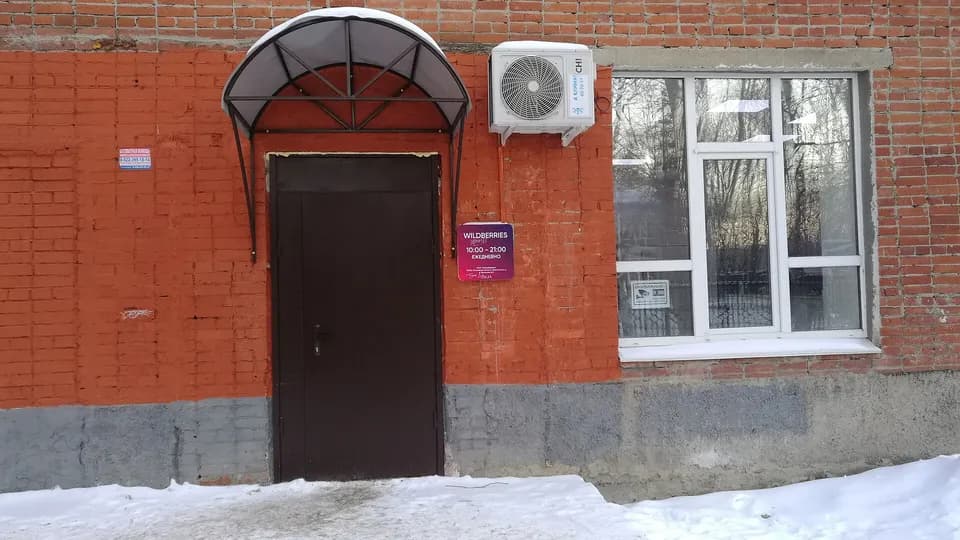 Вход в пункт выдачи Wildberries в кирпичном здании, над дверью козырёк, рядом табличка с логотипом