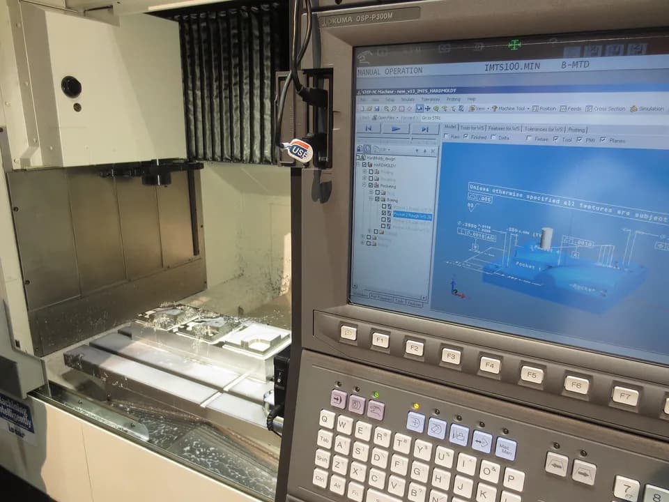 Рабочая зона фрезерного станка Okuma с заготовкой и стойка ЧПУ с моделью детали на экране