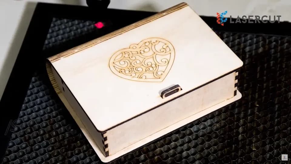 Фанерная шкатулка с резным сердцем на крышке, собранная на шипах, на столе лазерного станка