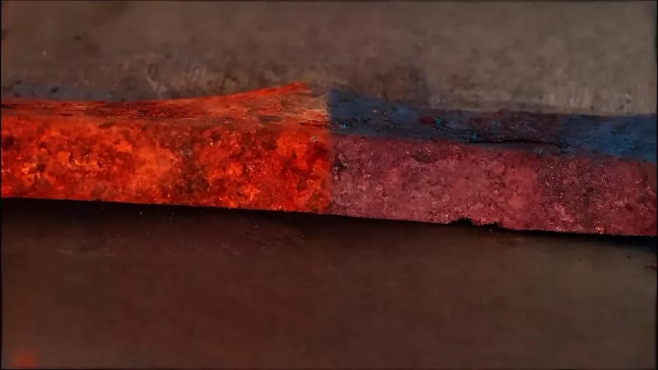 Крупный план торца металлической заготовки, на котором слой красного покрытия обрезан и виден синий слой под ним