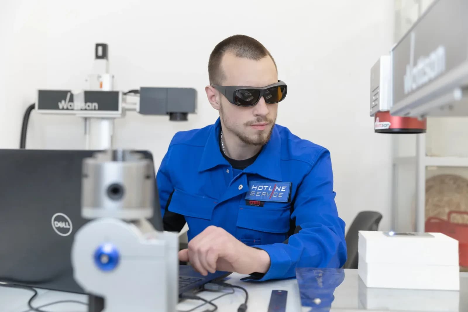 Оператор в защитных очках работает за ноутбуком рядом с лазерным маркером Wattsan