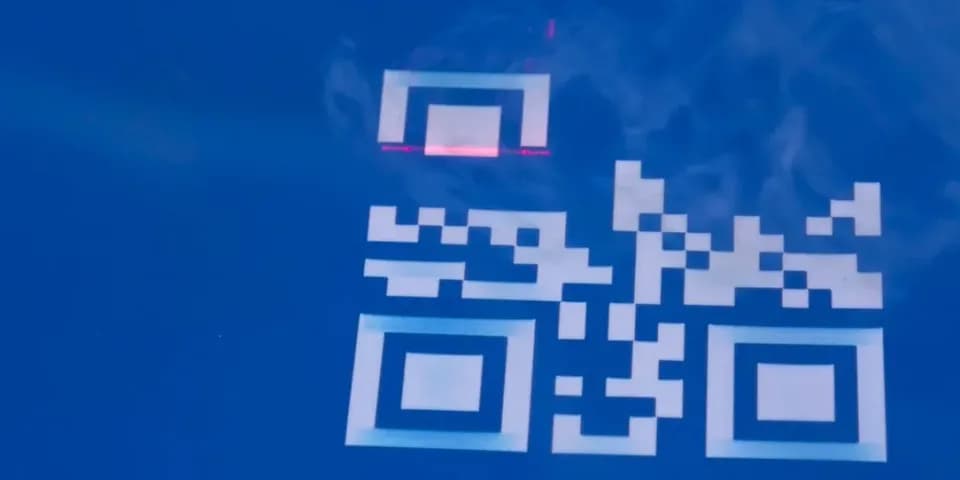 Крупный план лазерной гравировки QR-кода на светлой поверхности, красный указатель луча над квадратным кодом