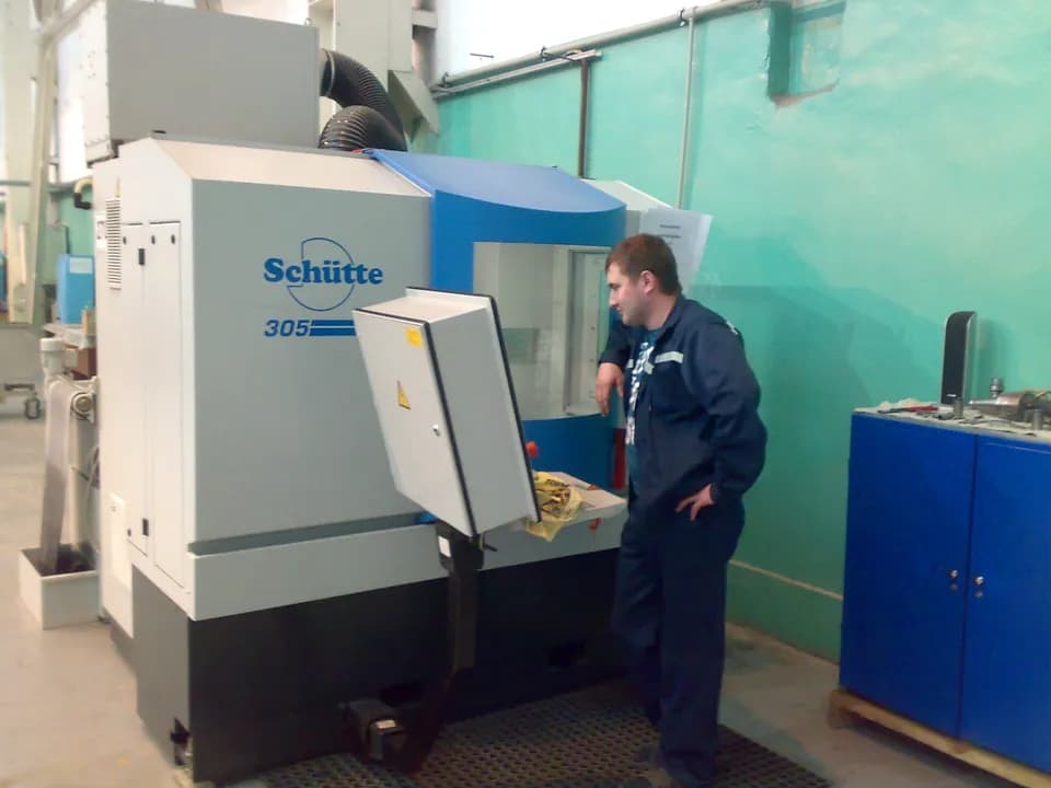 Оператор стоит у станка с ЧПУ Schütte 305 в цехе завода