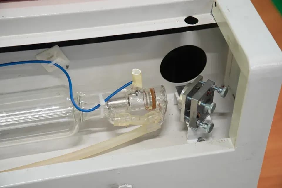 Стеклянная трубка CO2-лазера внутри корпуса станка с подключёнными водяными шлангами и юстировочным узлом справа