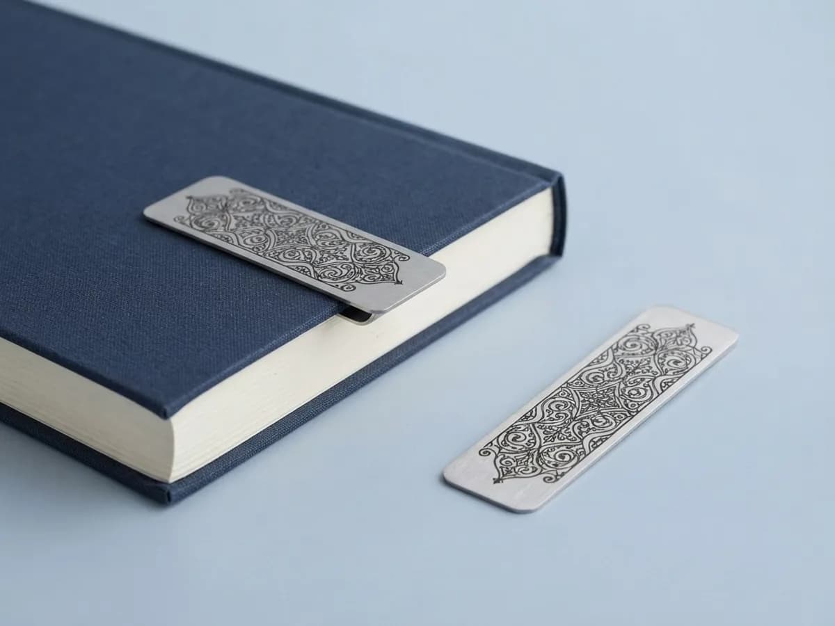Две тонкие стальные закладки с орнаментом, одна надета на край закрытой книги в тканевой обложке