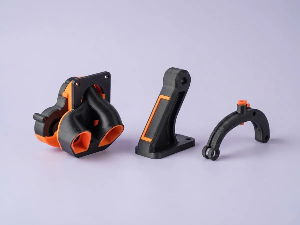 Напечатанные чёрно-оранжевые детали для 3D-принтера: воздуховод обдува, держатель катушки и направляющая нити